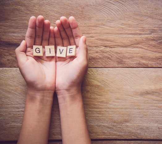 Hands holding wooden letter tiles that spell 'GIVE' on a wooden surface, symbolizing charity and generosity