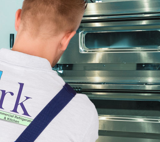 Technician inspecting a commercial kitchen oven, focusing on the stainless steel exterior and control panels.